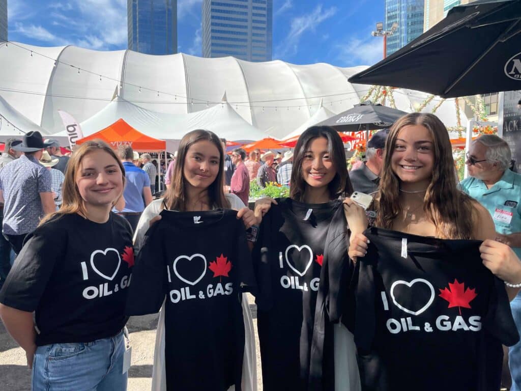Youthful advocates showing support for oil and gas industry at outdoor event, holding "I ❤️ Oil & Gas" shirts.