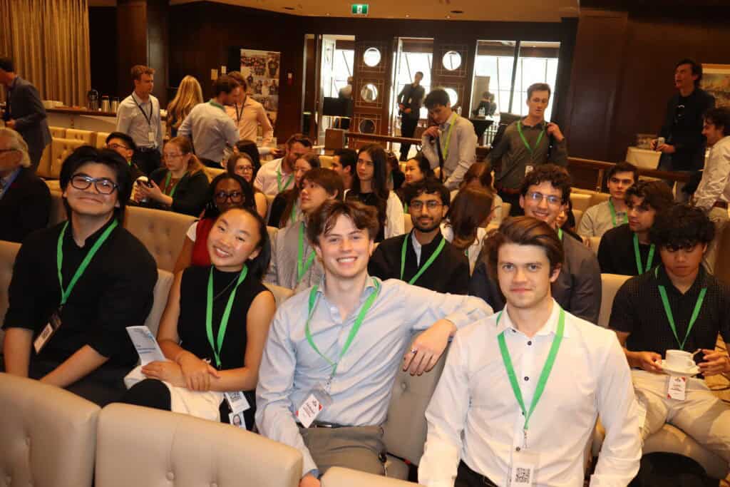 AI-generated group photo of young professionals attending a conference, featuring diverse individuals wearing ID badges in a warm, indoor setting filled with people, indicating a formal networking or seminar event.