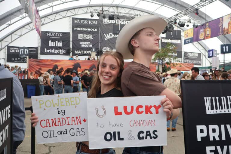 Young man and woman holding signs supporting Canadian oil and gas industry at an indoor event.